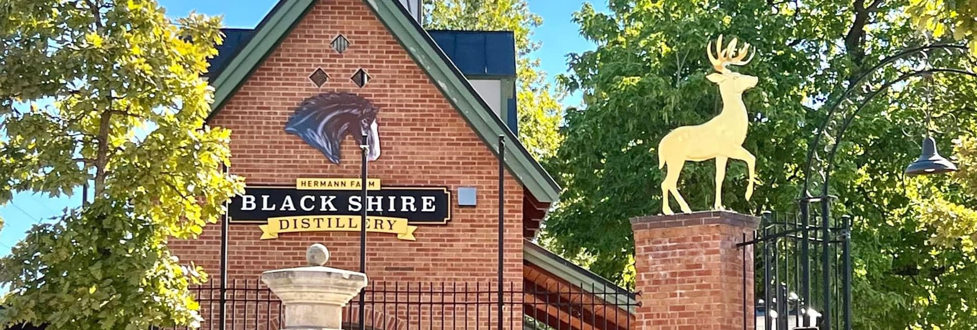 Exterior of Black Shire Distillery featuring a golden deer statue and greenery.