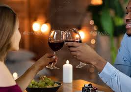 A couple toasts with glasses of red wine at a candlelit dinner.
