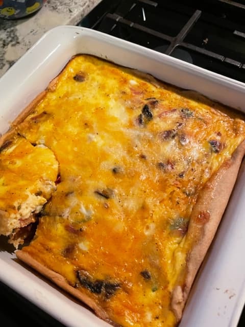 A square dish of baked frittata with a golden cheesy top, partially sliced.