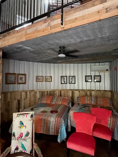 A cozy room featuring two beds, colorful quilts, a red chair, and framed artwork on the walls.