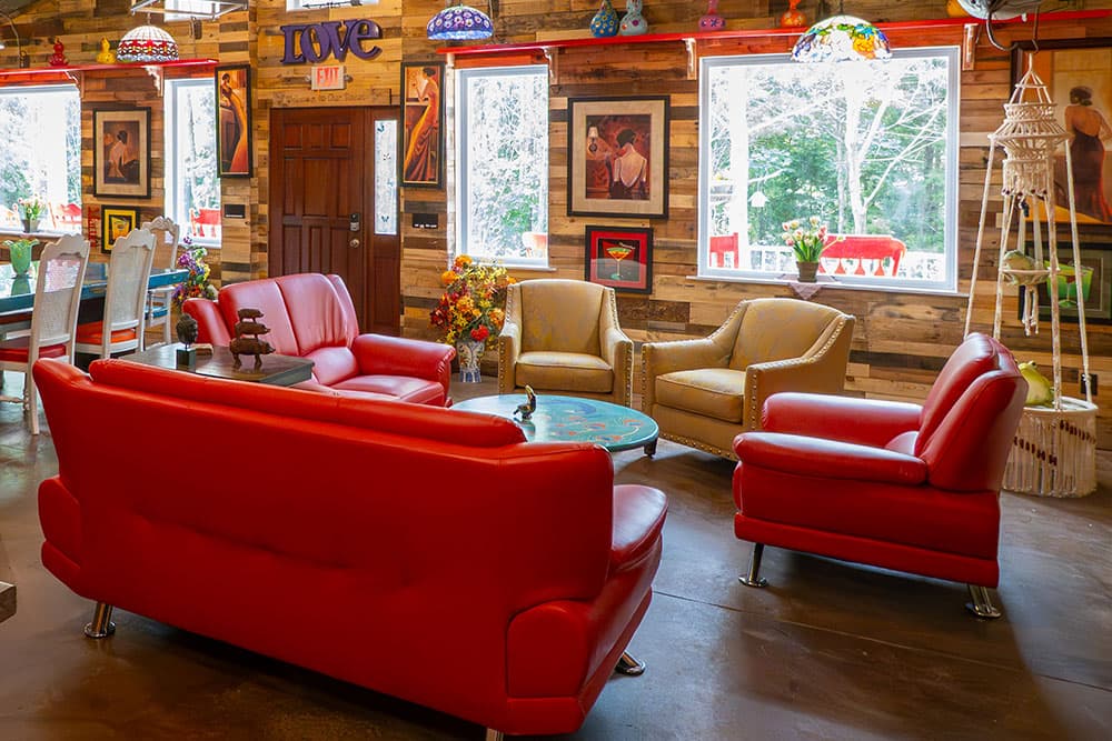 A cozy living room featuring red leather sofas, wicker chairs, and wooden walls adorned with colorful art.