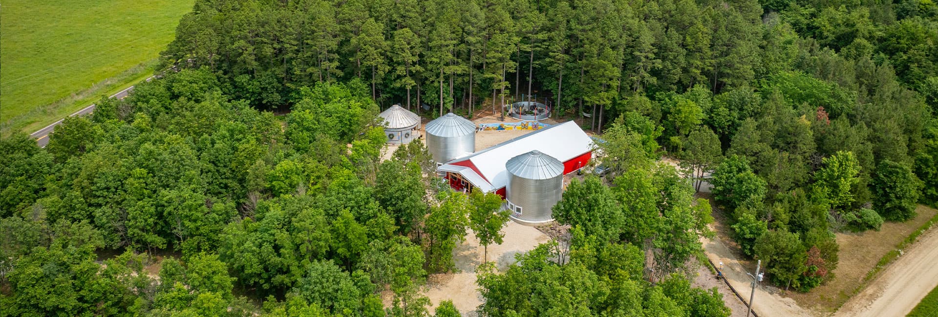 Aerial view of a red-roofed building and silos surrounded by dense trees.