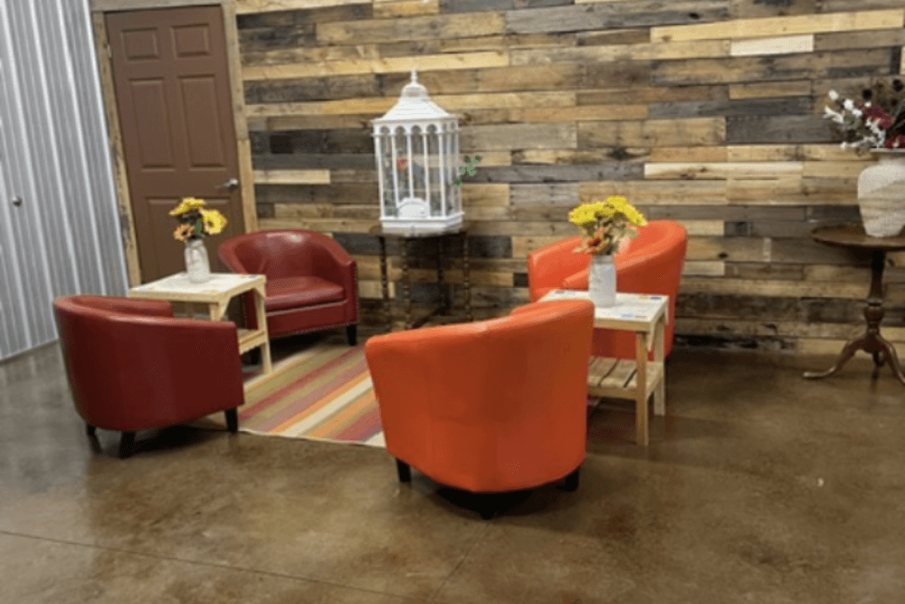 A cozy seating area with orange armchairs, small tables, floral arrangements, and a vintage birdcage against a wooden wall.