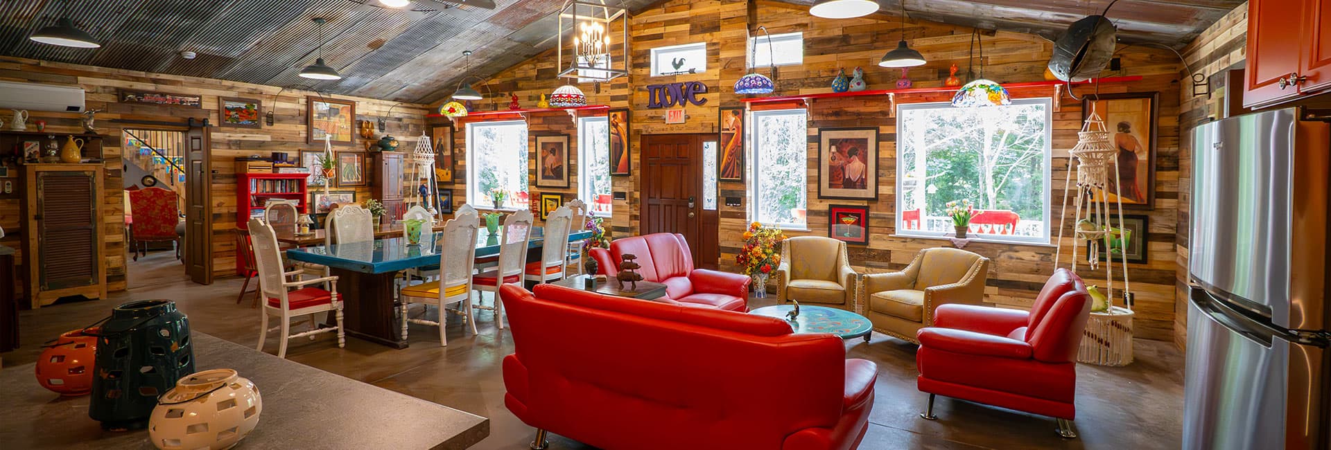 A cozy, rustic living space with colorful furniture, wood-paneled walls, and large windows letting in natural light.