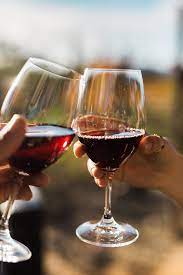 Two glasses of red wine clinking together against a blurred outdoor background.