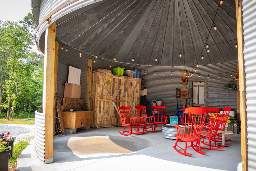 A circular, inviting gathering space featuring red rocking chairs, decorative items, and string lights.