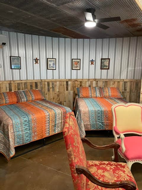 A cozy room featuring two beds with colorful patterned quilts and vintage-style chairs.
