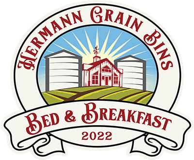 Logo for Hermann Grain Bins Bed & Breakfast featuring silos and a farmhouse with rays of sunlight.