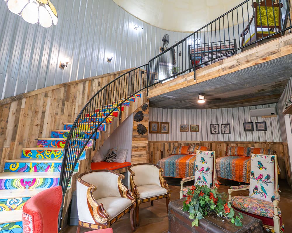 Colorful interior of a modern rustic room featuring a spiral staircase, patterned bedding, and vintage furniture.