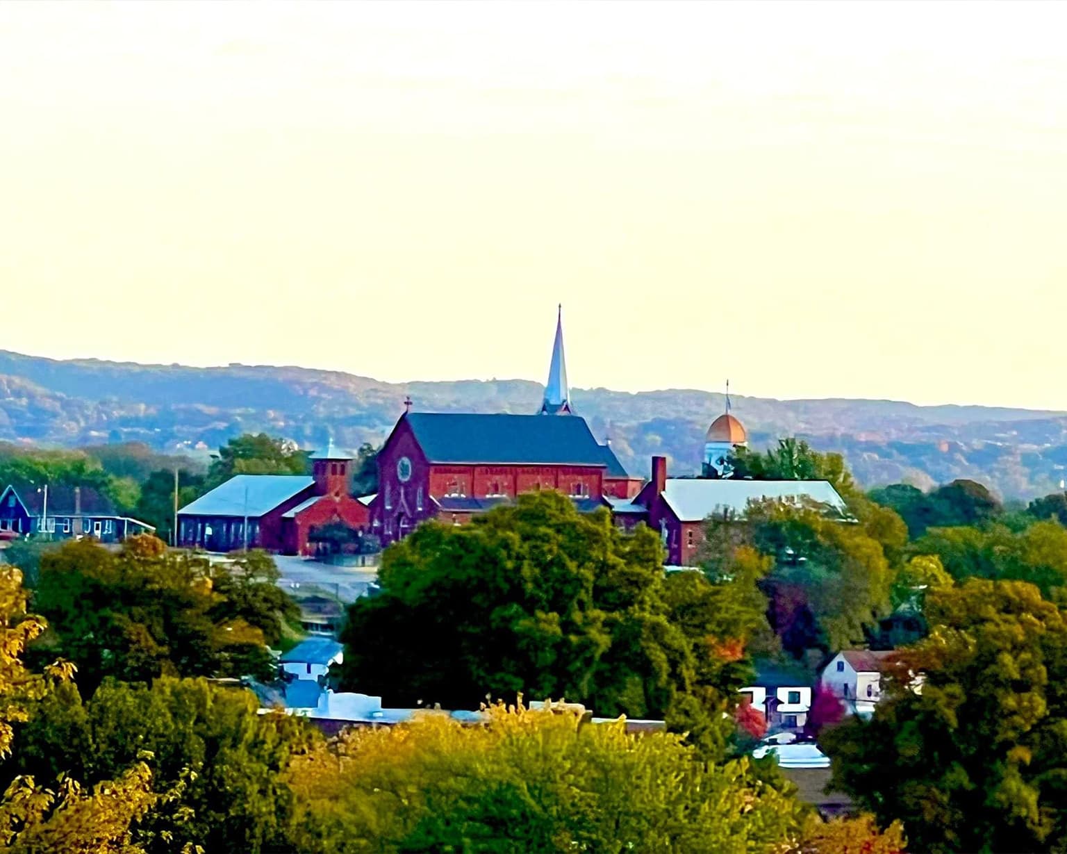 A panoramic view of a town with a prominent church steeple and lush greenery in the foreground.